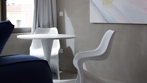 A modern room with a round table and two white chairs, a large abstract painting on the wall, and a view of buildings outside the window. - 99 Adrianou Luxury Urban Stay (Athens)