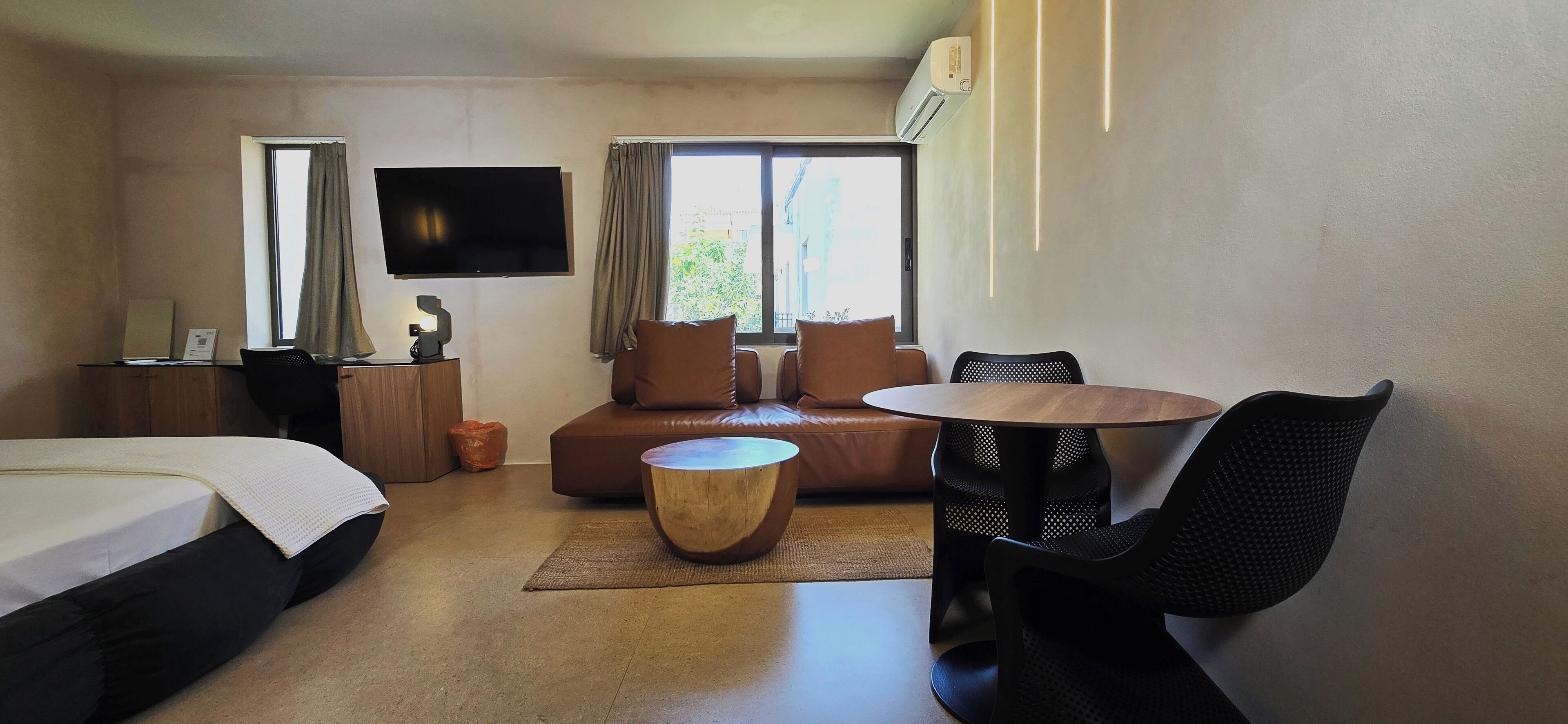 A hotel room with a bed, a sofa, a dining table, a TV, and a window with curtains.