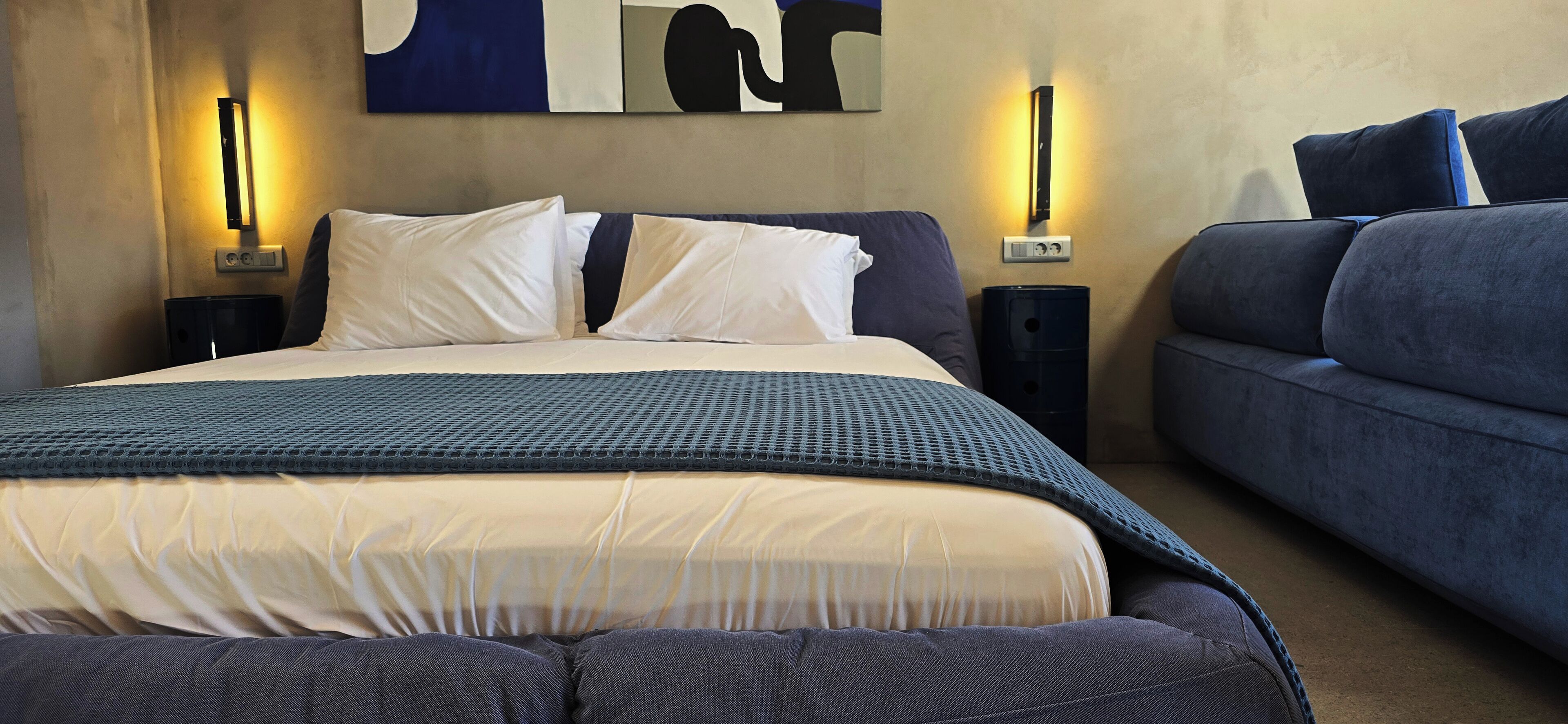 A hotel room with a large bed, two bedside tables, a sofa, and wall-mounted lighting.