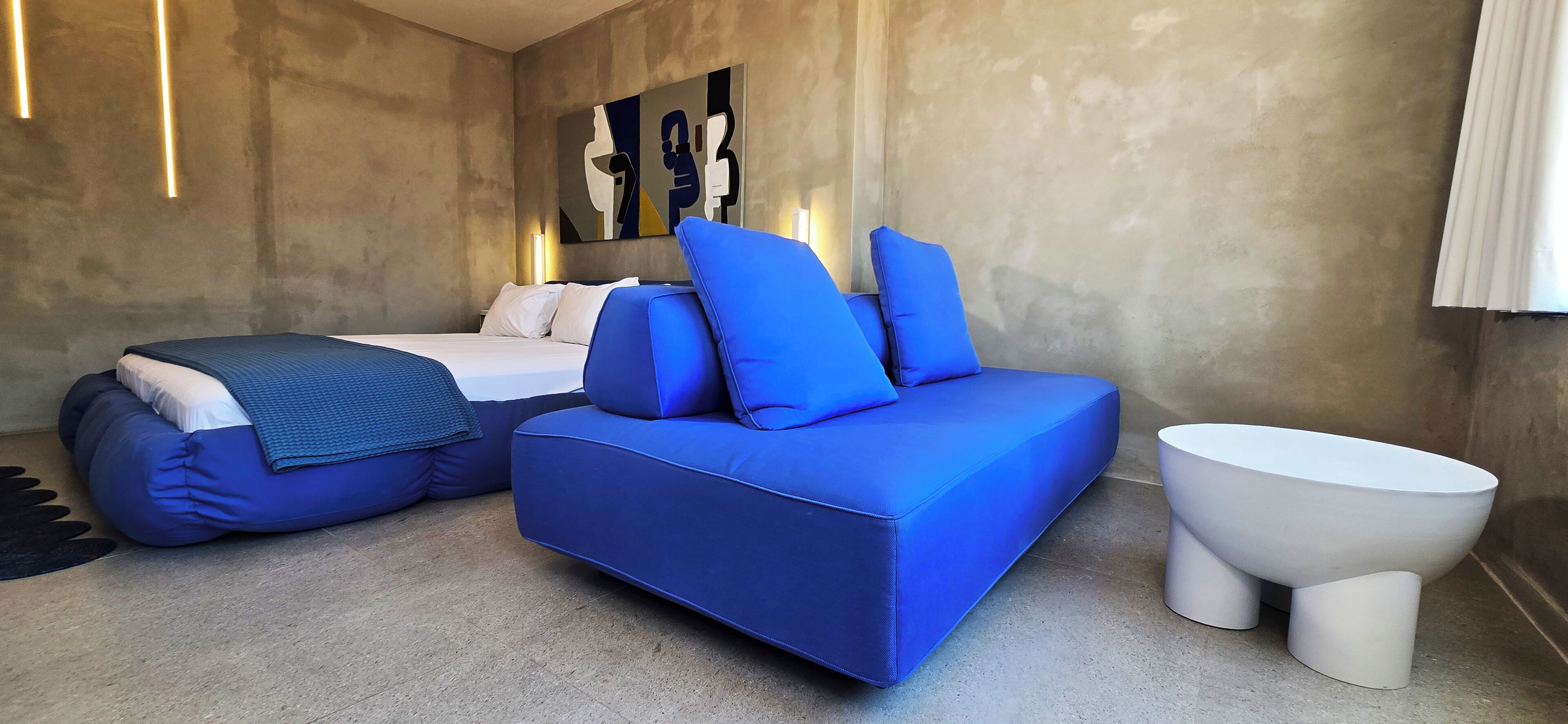 Un dormitorio moderno con una cama, un sofá azul, un inodoro blanco y una obra de arte en la pared.