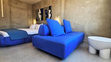 Un dormitorio moderno con una cama, un sofá azul, un inodoro blanco y una obra de arte en la pared.
