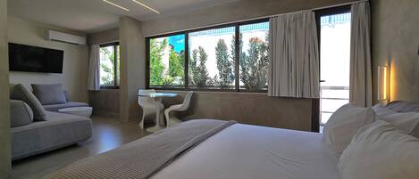 A modern hotel room with a large bed, a sofa, a small table, and a TV.