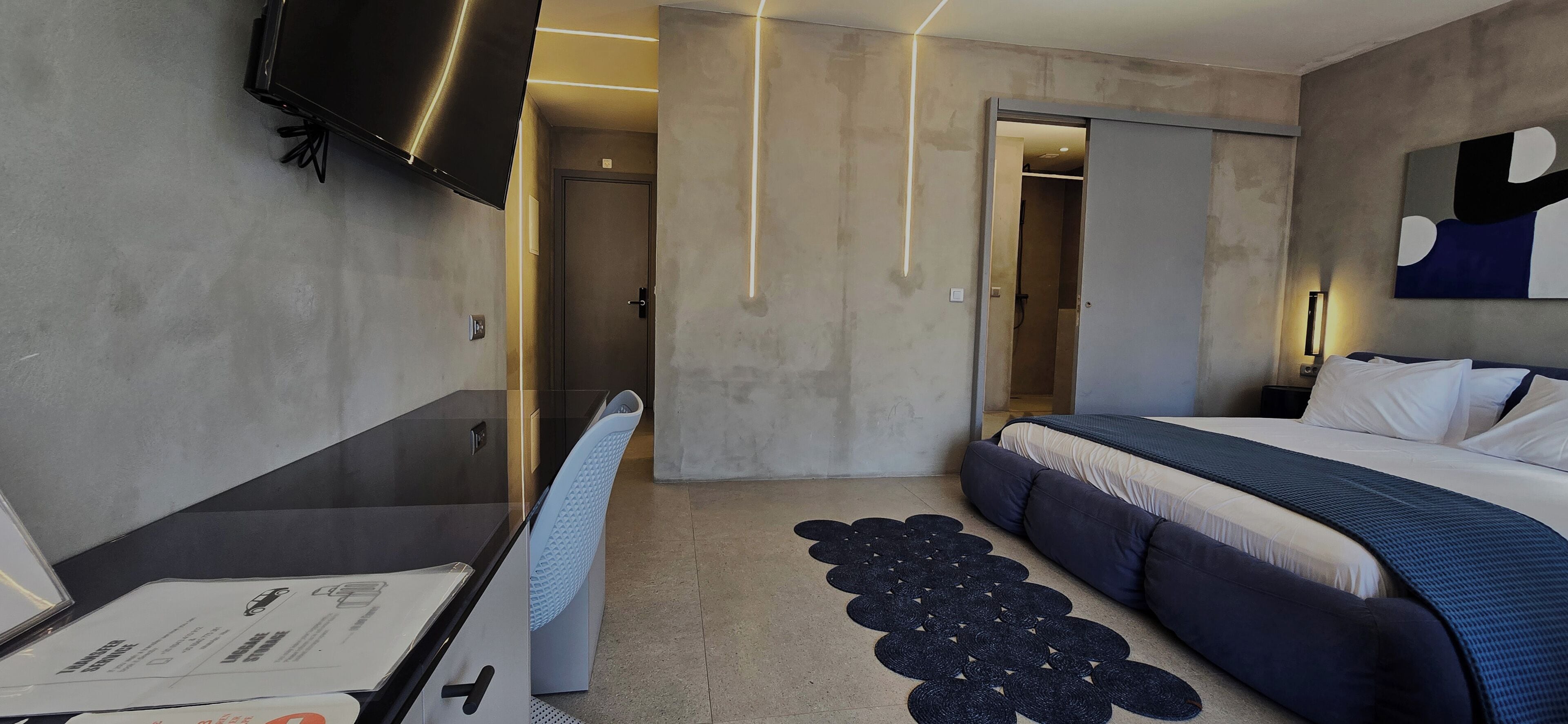 A modern hotel room with a bed, a desk, a flat-screen TV, and a door leading to a bathroom.