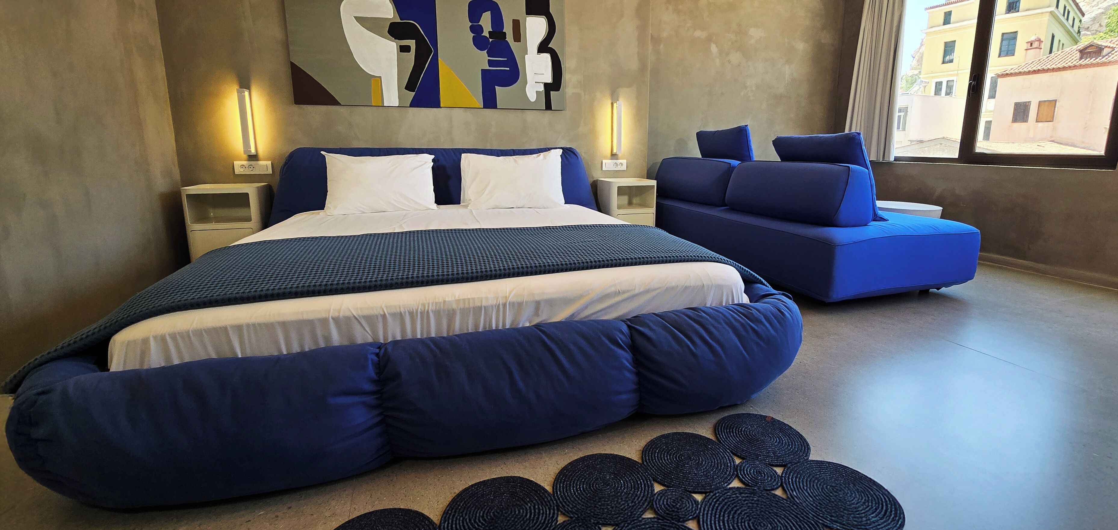 Ein modernes Schlafzimmer mit einem großen Bett, einem Schlafsofa und einem an der Wand befestigten Kunstwerk.