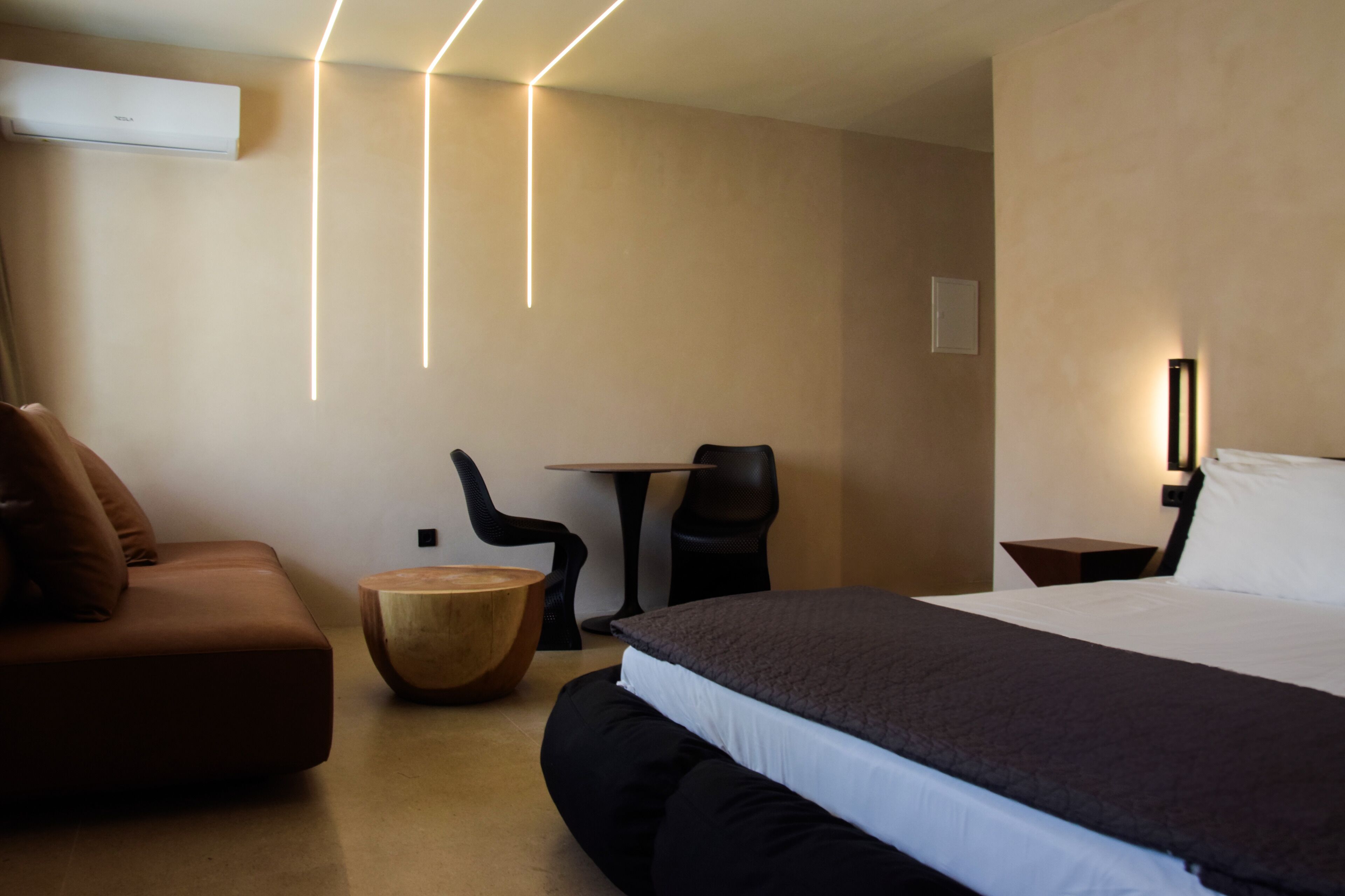 A modern hotel room with a large bed, a sofa, a wooden side table, and a small round table.