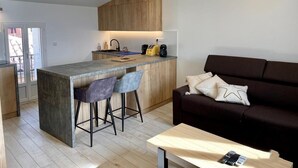 Une cuisine moderne avec un îlot central, des tabourets de bar, un canapé brun foncé et une table basse en bois.