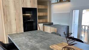 Une cuisine moderne dotée d’un grand îlot central, d’appareils électroménagers intégrés et offrant une vue à travers une porte vitrée.