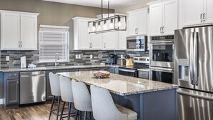 A modern kitchen with stainless steel appliances, white cabinetry, and a granite countertop.