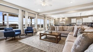 A spacious living room with a large sofa, two armchairs, a coffee table, and a view of the outdoors through large windows.
