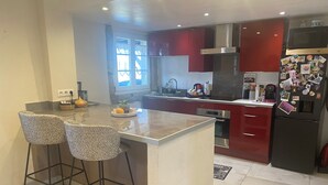 A modern kitchen with a central island, red cabinets, stainless steel appliances, and two bar stools. - Appartement Entier, Comme un Loft, Chez Ariane on sy Sent Bien ! (Mittersheim)
