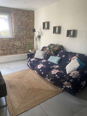 A living room with a stone wall, a sofa with floral upholstery, a woven rug, and a window with a view.
