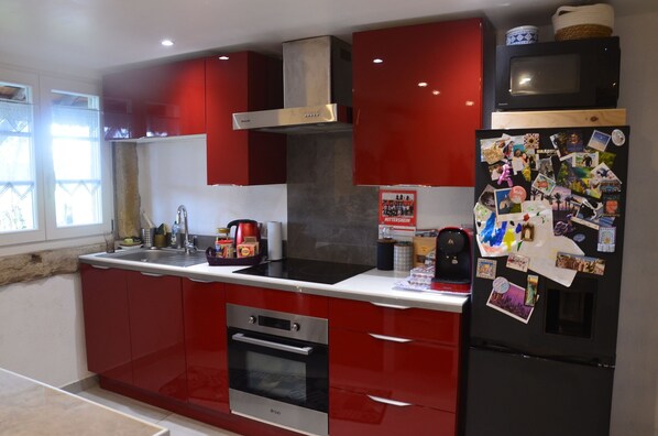 A modern kitchen with red cabinets, stainless steel appliances, and a refrigerator covered in photos. - Appartement Entier, Comme un Loft, Chez Ariane on sy Sent Bien ! (Mittersheim)
