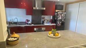 A modern kitchen with red cabinets, a stainless steel range hood, a microwave, and a refrigerator with magnets. There is a marble countertop with a fruit bowl and a woven basket. - Appartement Entier, Comme un Loft, Chez Ariane on sy Sent Bien ! (Mittersheim)