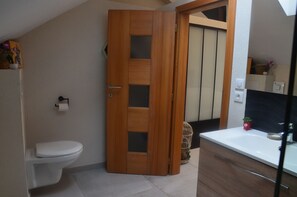 A bathroom with a wooden door, a white toilet, a sink with a mirror, and a small potted plant.