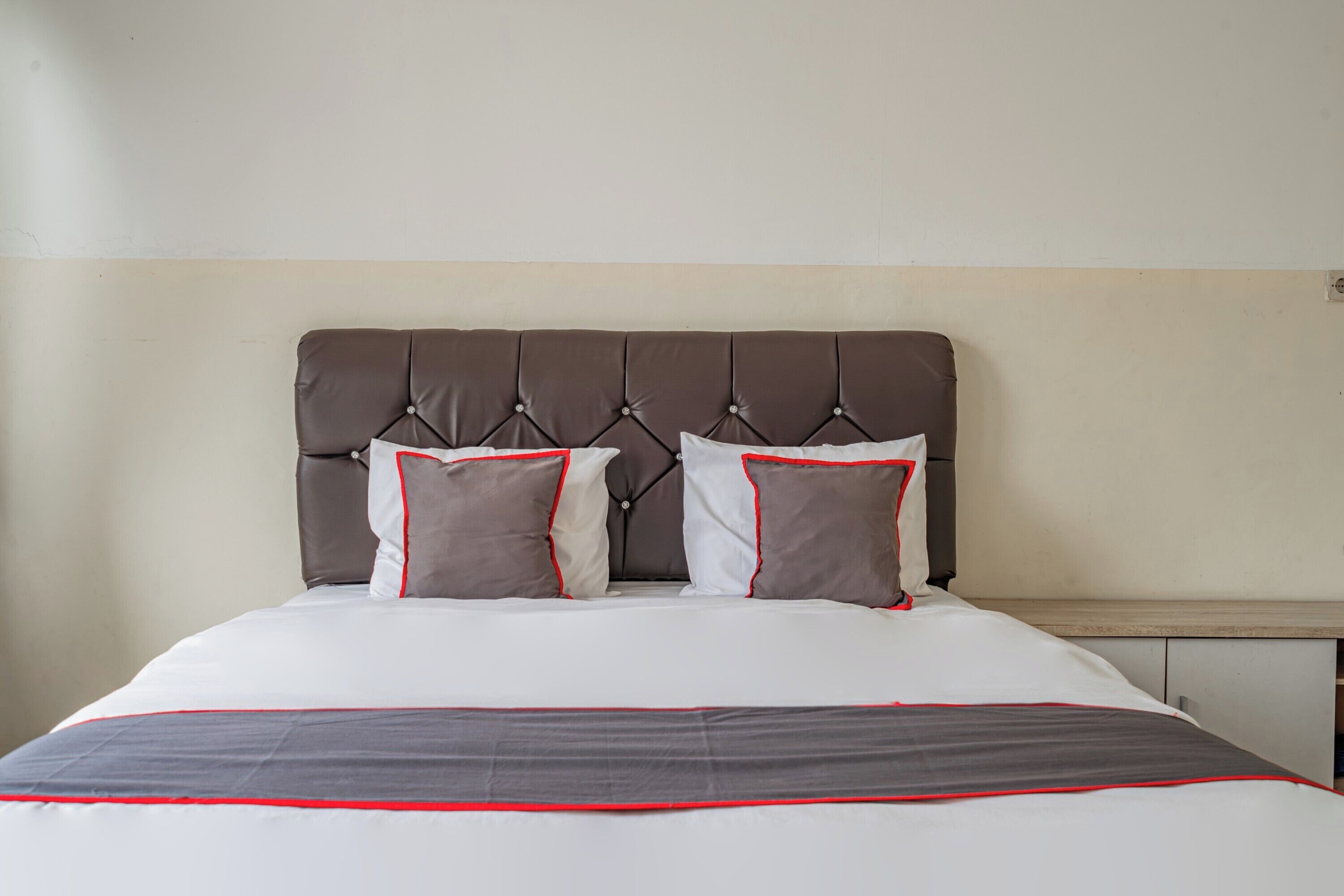 A neatly made bed with a tufted headboard, two pillows, and a grey and red bedspread.