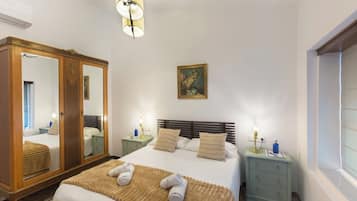 A bedroom with a large mirror, a bed with white linens, two bedside tables with lamps, and a window with blinds.