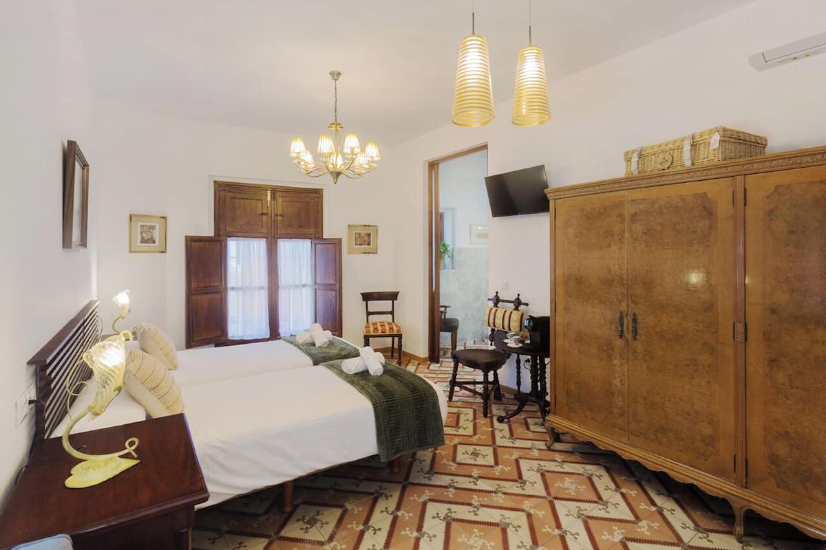 Een hotelkamer met een bed, een houten kledingkast, een bureau met stoel, een televisie en een kroonluchter.
