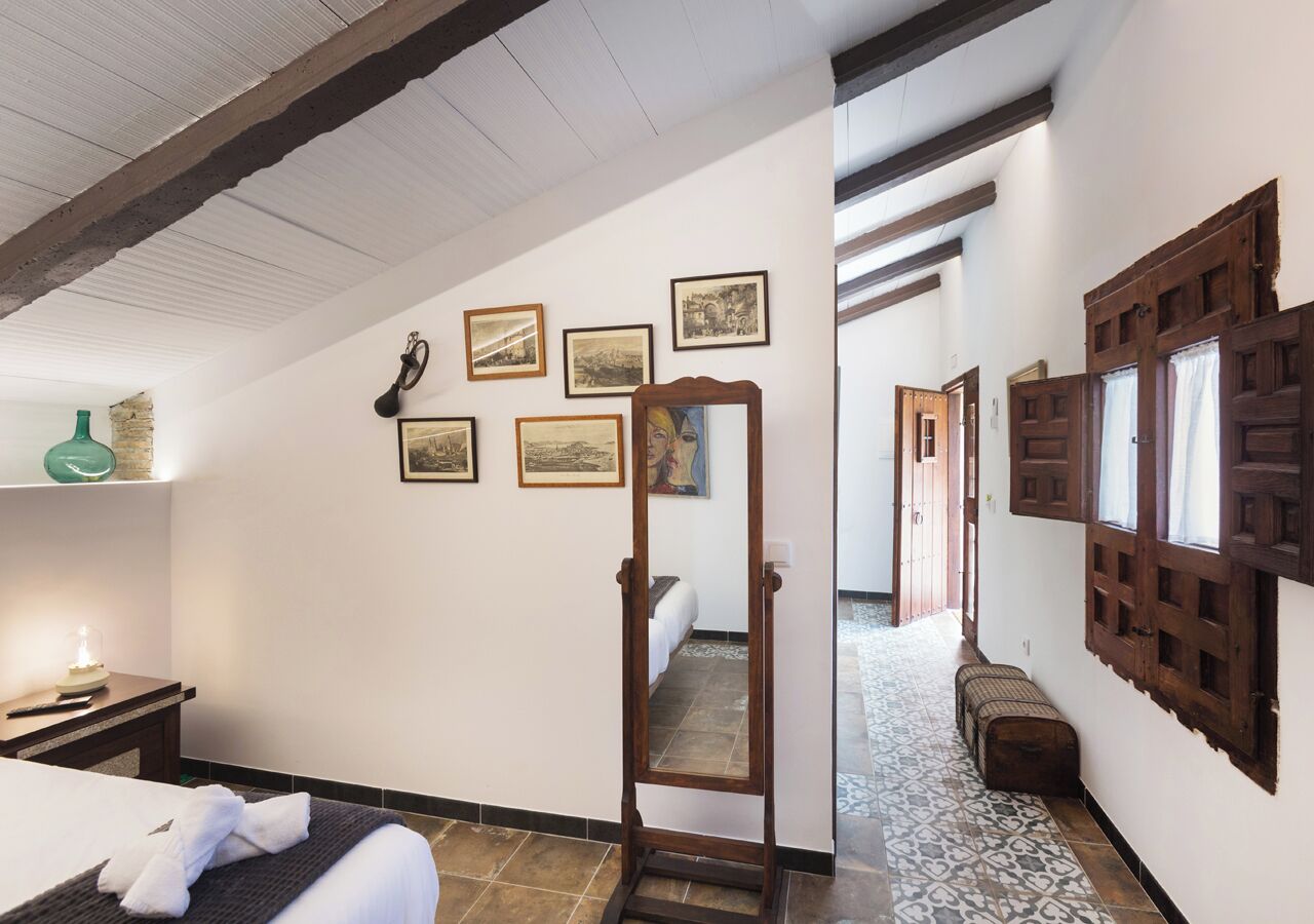A hotel room with a bed, a bedside table with a lamp, a mirror, and framed pictures on the wall.