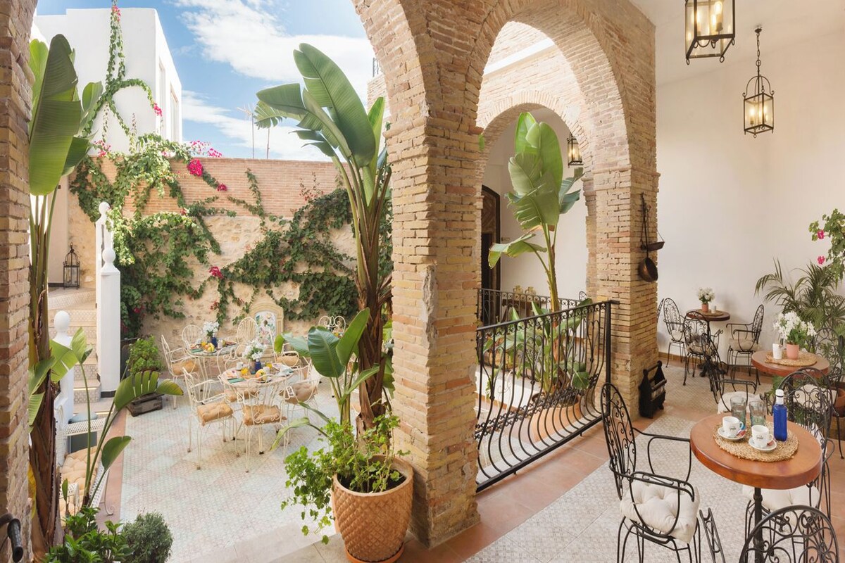 Un patio al aire libre con arcos de ladrillo, plantas en macetas y mobiliario de metal.