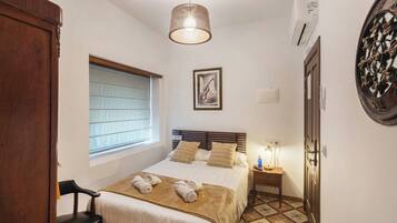 A bedroom with a bed, a nightstand, a chair, a window, and a door.