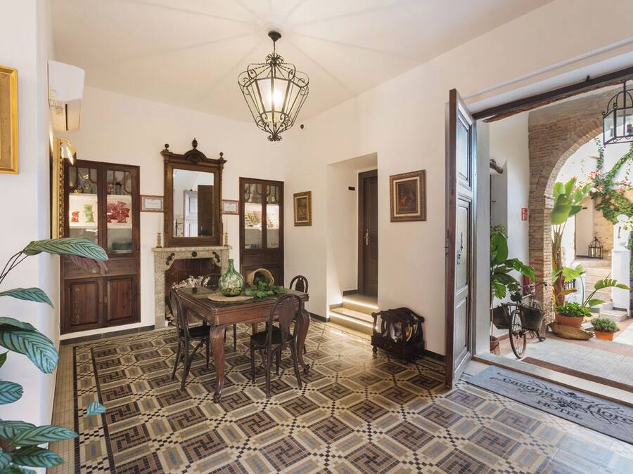 A dining area with a patterned floor, a chandelier, and a view of the outdoor garden through an open doorway.