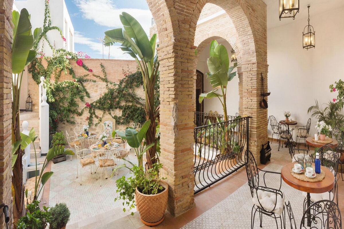 Un patio con arcos de ladrillo, plantas en macetas y mobiliario exterior.