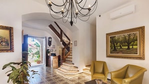 A spacious lobby with a patterned floor, a staircase, a chandelier, and a large painting. - La Casona de las Flores (Ondara)