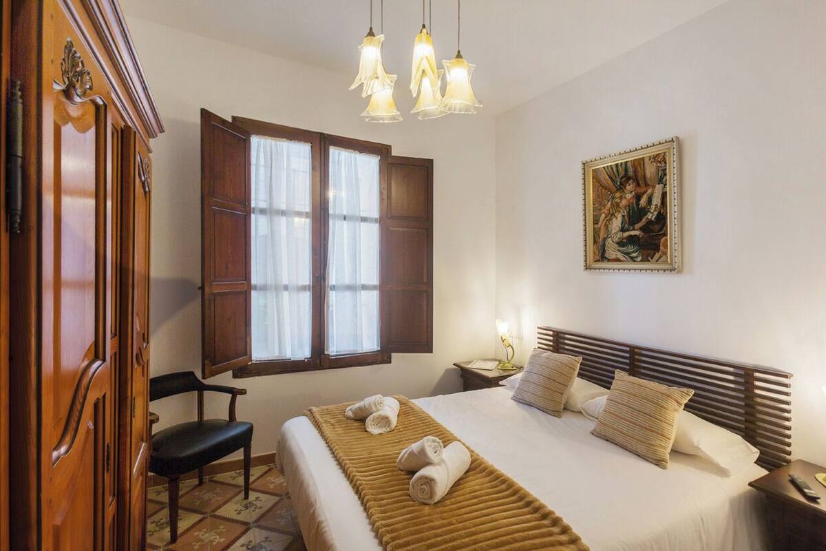 Een hotelkamer met een bed, een stoel, een kast, een schilderij en een raam met gordijnen.