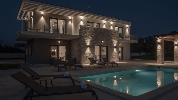 Une maison moderne à deux étages, dotée d’une piscine, d’un espace extérieur aménagé et d’une façade en pierre.