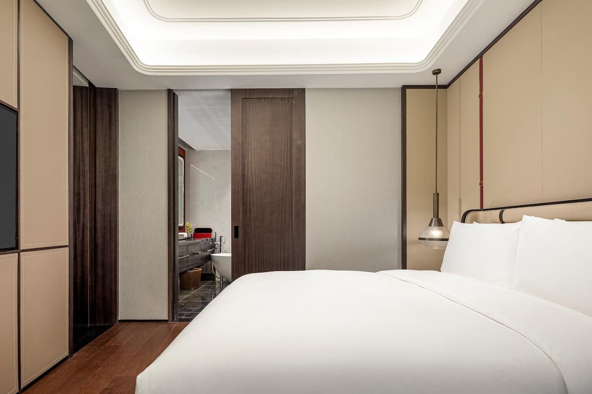 Een moderne hotelkamer met een groot bed, een kaptafel met spiegel en een plafondlamp.