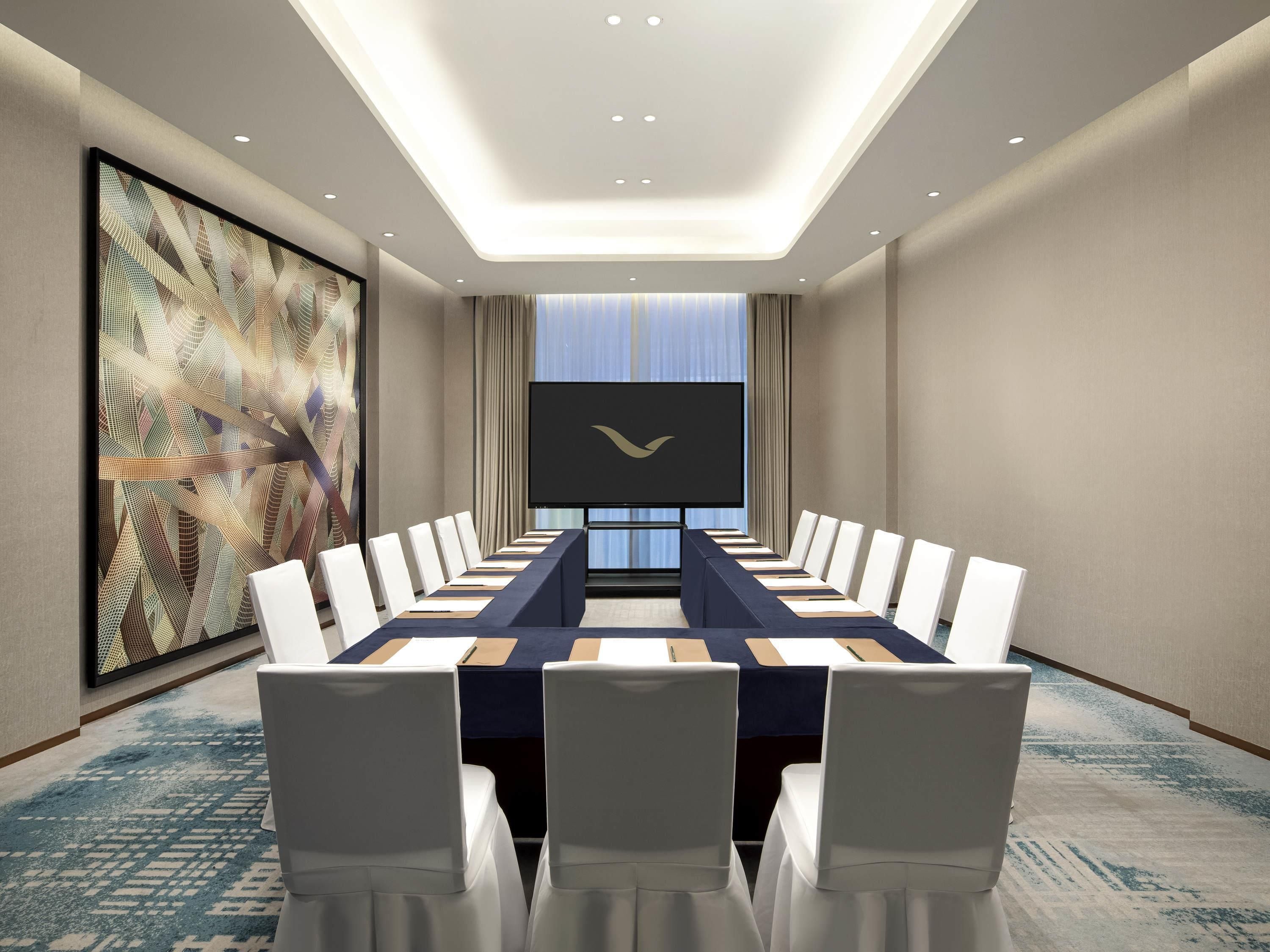 Una sala de conferències amb una taula llarga, cadires blanques i una pantalla gran.