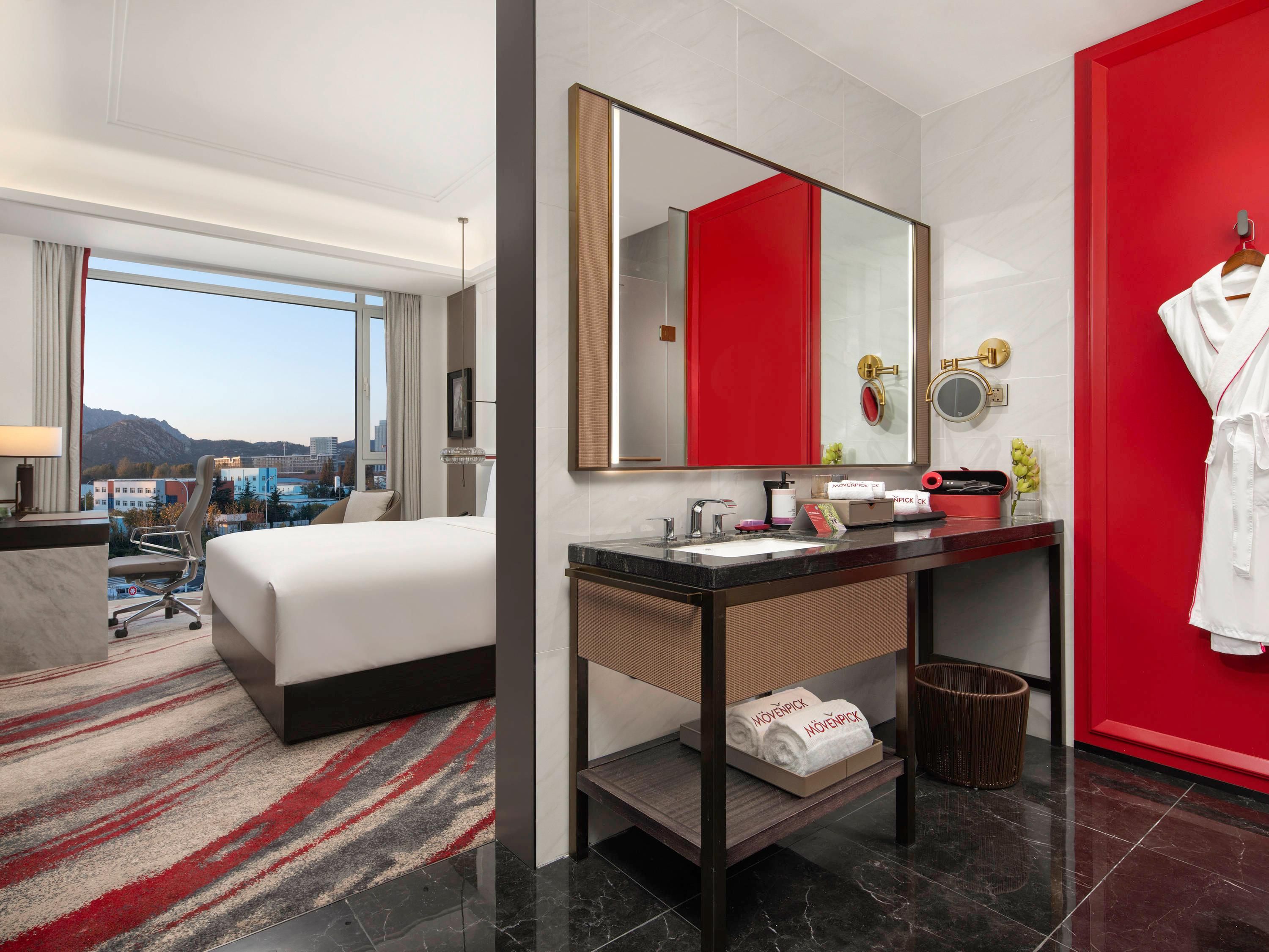 Ein Hotelzimmer mit Bett, Schreibtisch, Badezimmer mit Spiegel und Blick auf die Stadt.