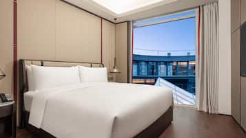 A modern hotel room with a large bed, a bedside table with a phone, and a view of a building through a window.
