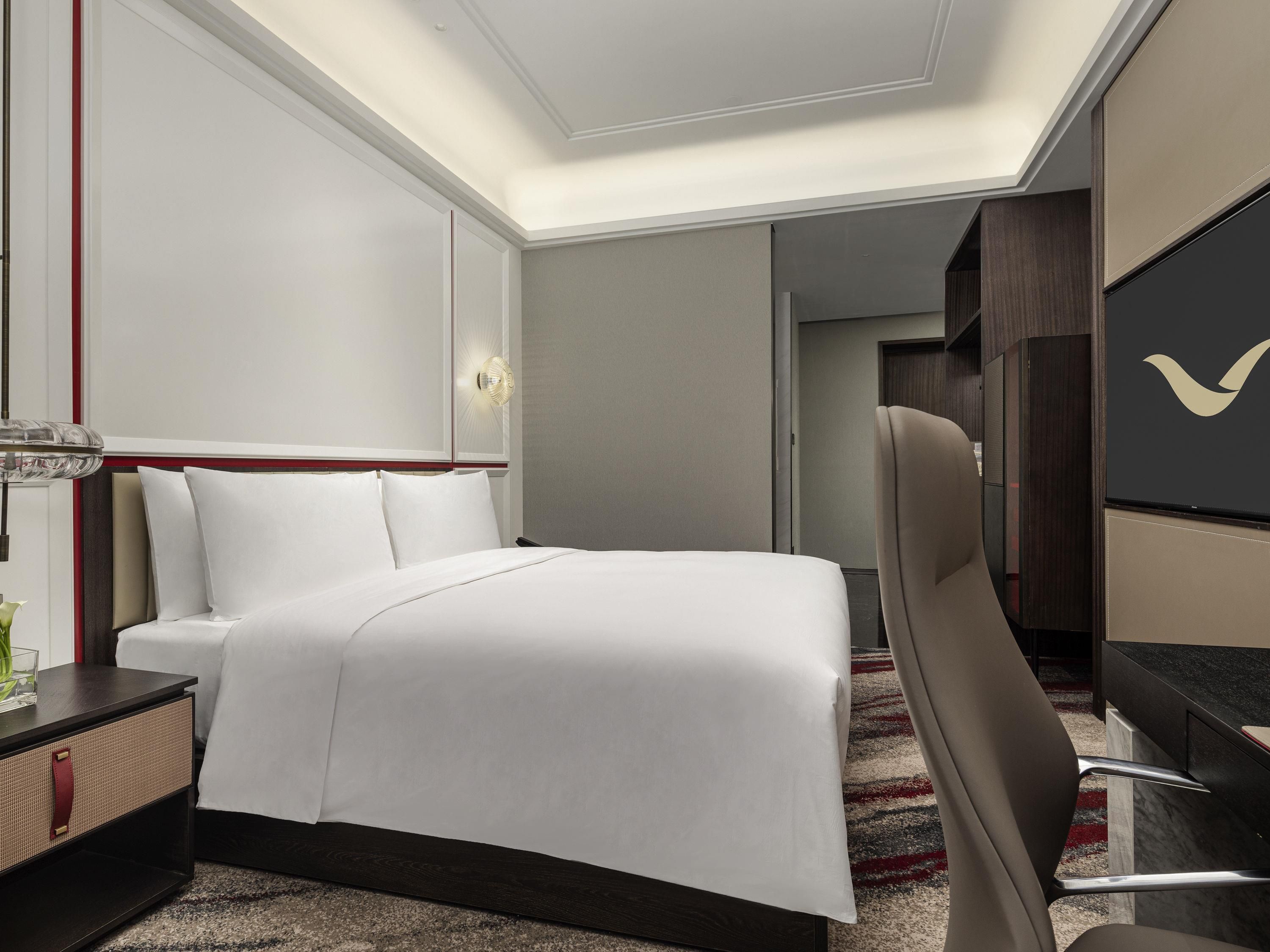 A hotel room with a bed, bedside table, chair, desk, and a large mirror.