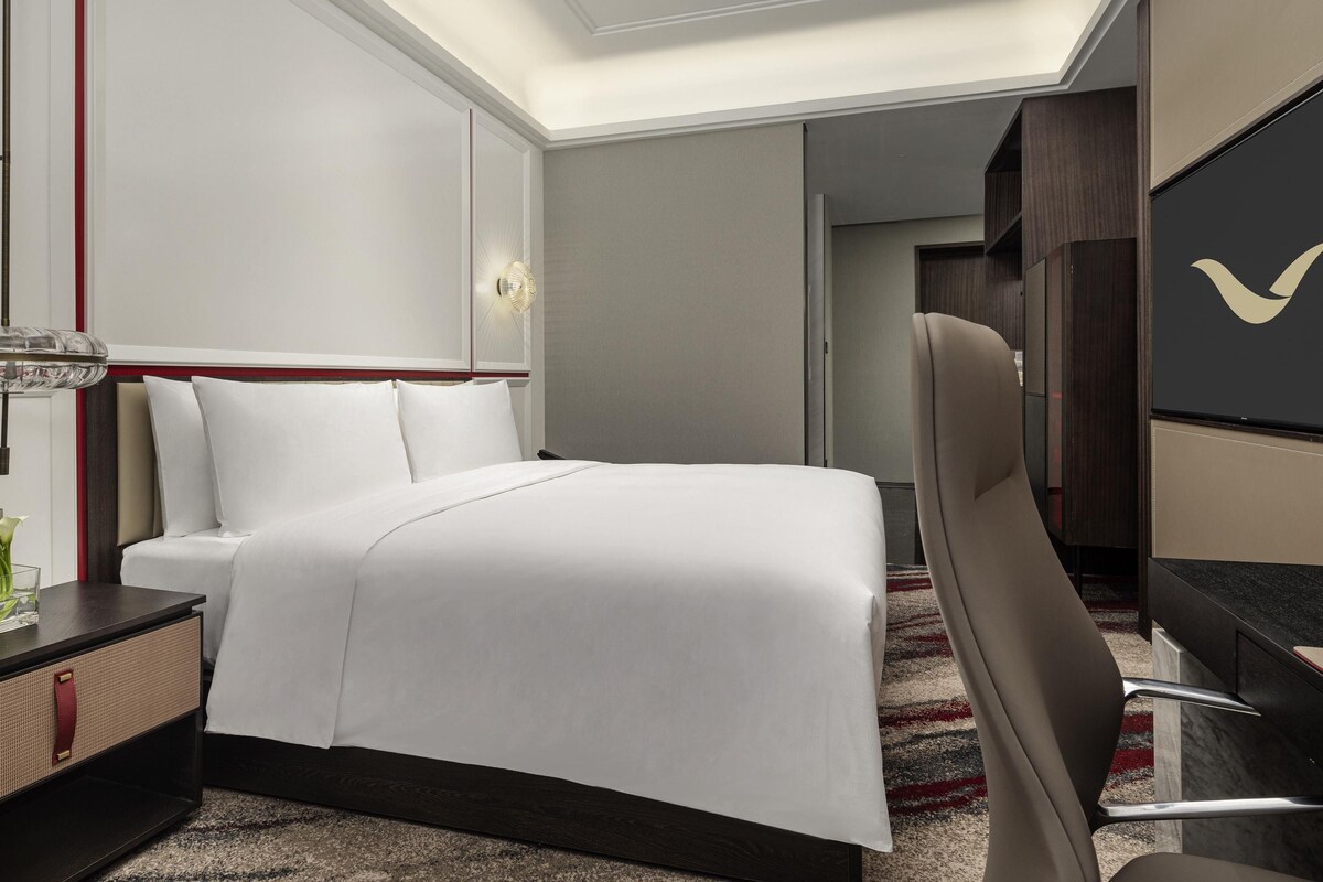 A hotel room with a bed, bedside table, chair, desk, and a large mirror.