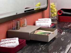 A hotel room with a marble countertop, a mirror, a red tray with a towel, a glass, and a box with a magazine. - Movenpick Qingdao Sunmei (Qingdao)