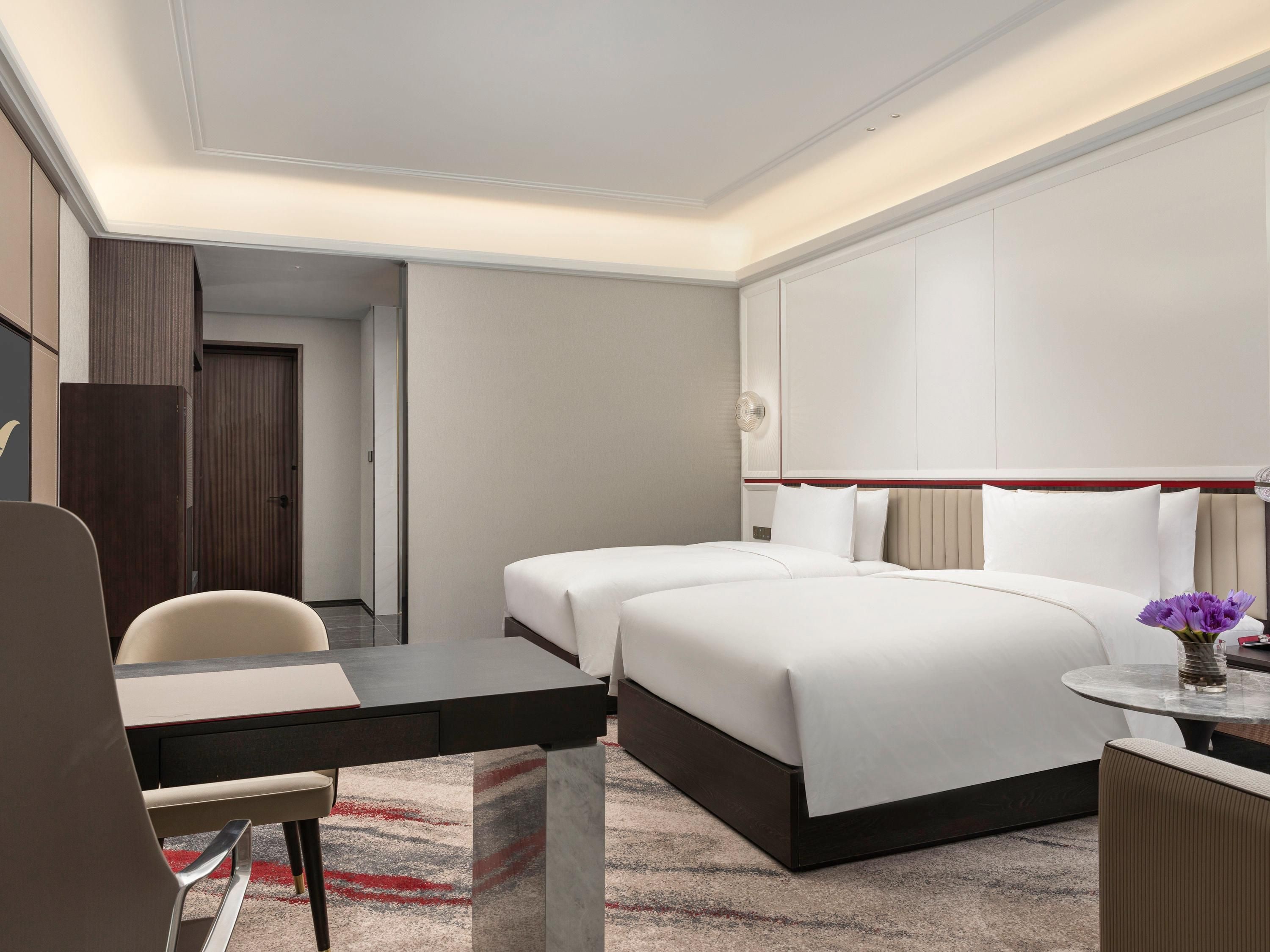 Habitació d'hotel amb un llit, un escriptori, una cadira i una taula petita amb un ram de flors.
