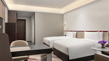 Habitació d'hotel amb un llit, un escriptori, una cadira i una taula petita amb un ram de flors.