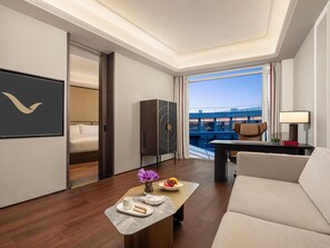 Une chambre d’hôtel moderne, équipée d’un lit, d’un bureau avec une lampe, d’un canapé et offrant une vue sur un immeuble grâce à de grandes fenêtres.