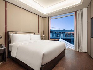 A hotel room with a large bed, a bedside table with a phone, a window with curtains, and a view of a building outside. - Movenpick Qingdao Sunmei (Qingdao)