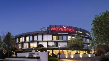 A modern building with a curved facade, large windows, and a prominent sign reading "MÖVENPICK by ACCOR".