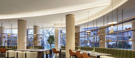 A modern hotel lobby with a curved ceiling, marble flooring, and a seating area with a green upholstered bench.
