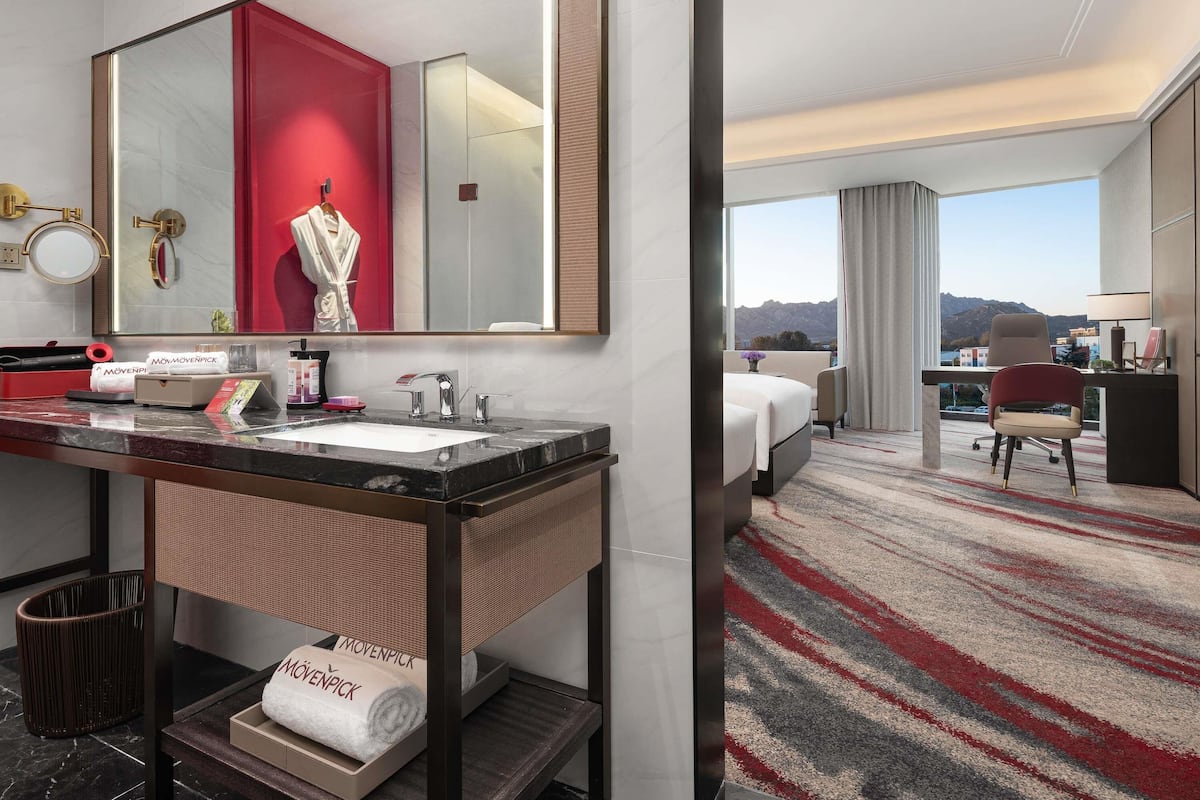 Hotelkamer met een grote spiegel, een wastafelmeubel met een wastafel, een bed, een bureau met een stoel en uitzicht op bergen.
