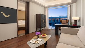 Ein modernes Hotelzimmer mit Bett, Schreibtisch, Sofa und Blick auf ein Gebäude durch große Fenster.
