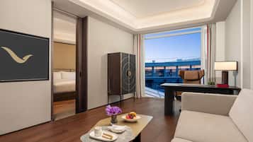 Ein modernes Hotelzimmer mit Bett, Schreibtisch, Sofa und Blick auf ein Gebäude durch große Fenster.