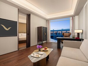 A modern hotel room with a bed, a desk, a sofa, and a view of a building through large windows. - Movenpick Qingdao Sunmei (Qingdao)