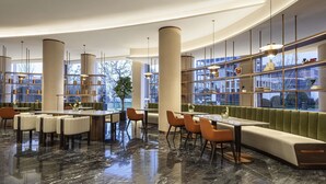 A modern hotel lobby with a curved ceiling, marble flooring, and a seating area with a green upholstered bench. - Movenpick Qingdao Sunmei (Qingdao)