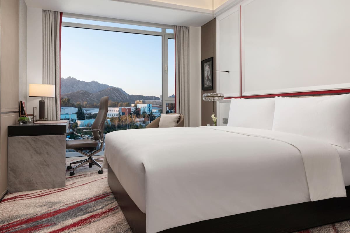 Hotelkamer met een groot bed, een bureau, een stoel en uitzicht op bergen en gebouwen.