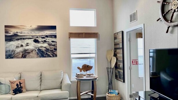A living room with a sofa, a television, a ceiling fan, a ship's wheel decoration, and a window with blinds. - 🛟🎣😎Harbor Lite 2BdrmDreamHouse +Loft! AT the PORT. Peeks of Harbor,River,Ocean! (Brookings)