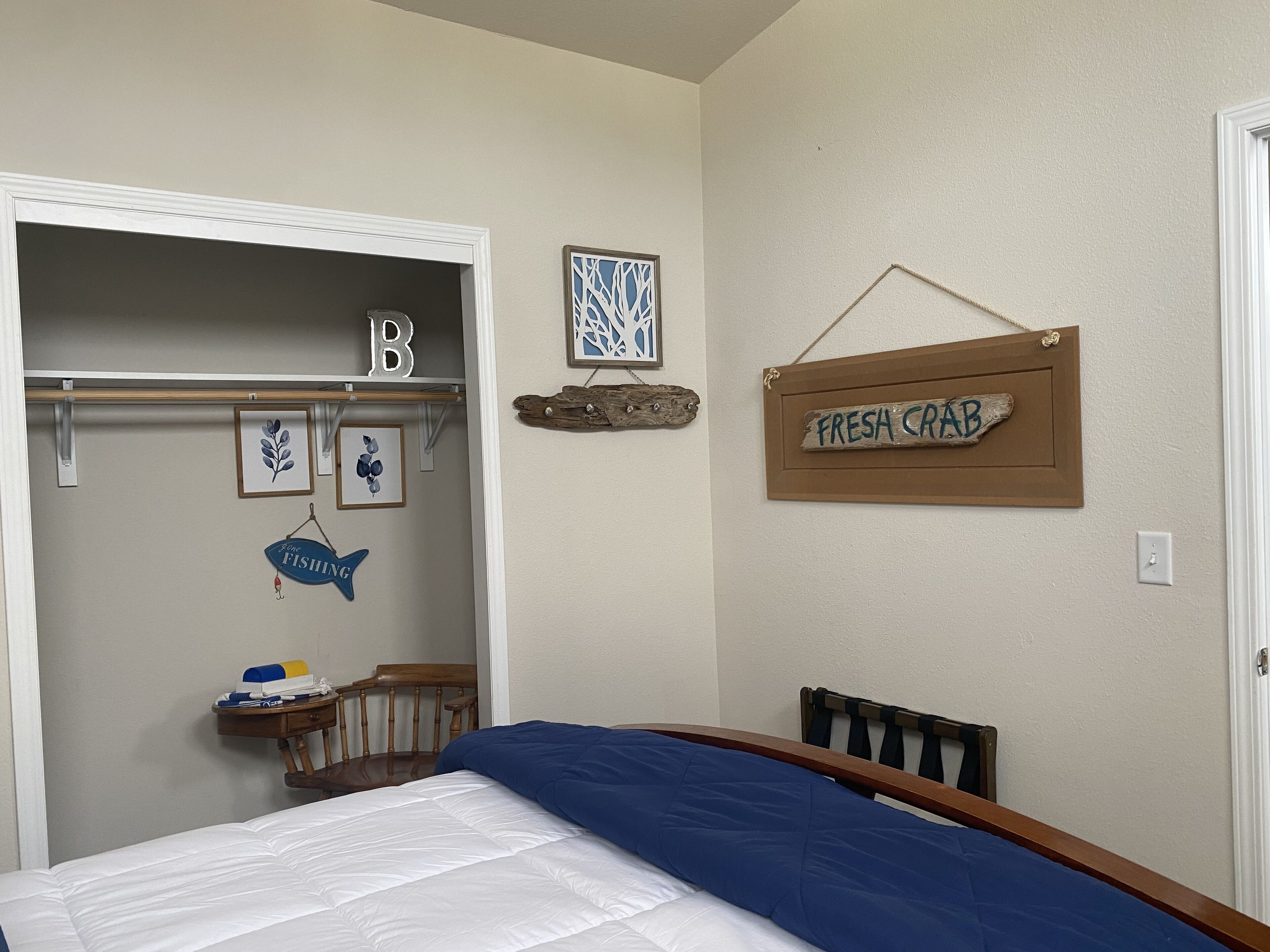 Un dormitorio con cama, cabecera de madera, mesita de noche, una silla, perchero y una pared con letrero que dice 'Fresh Crab'.